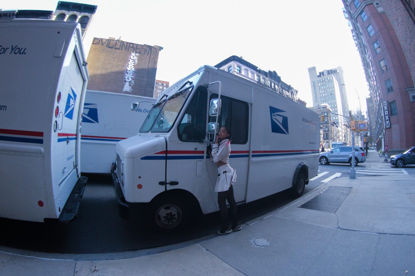 Hailey beside a row of mail trucks on a New York corner